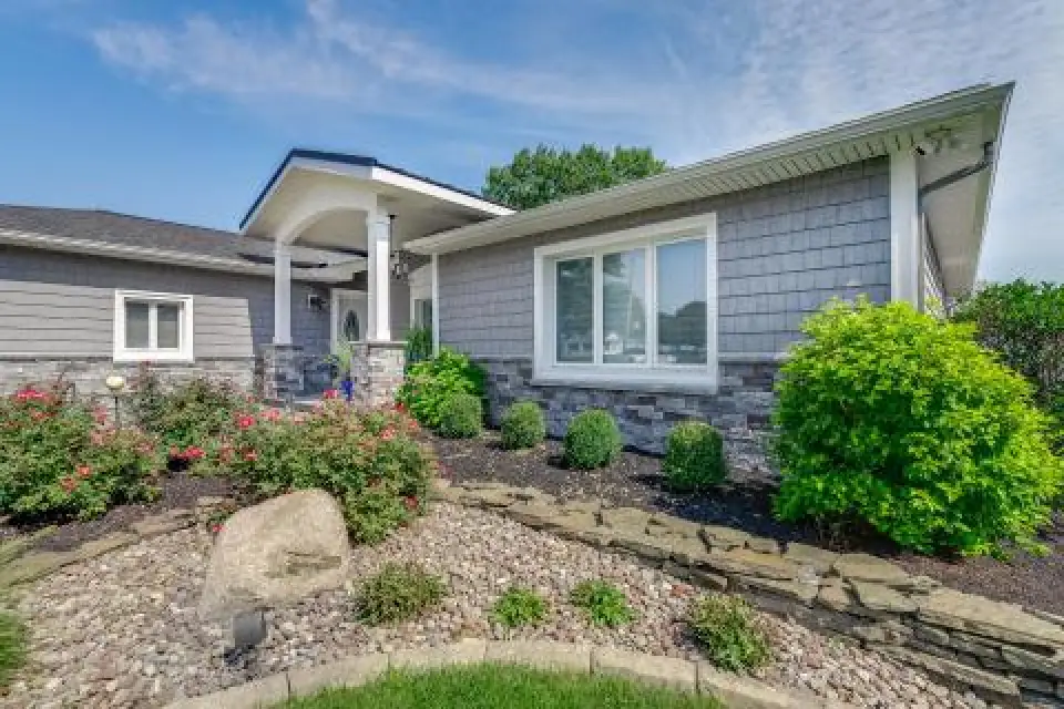 Single-story gray house with white trim, surrounded by shrubs, flowers, and a rock garden.