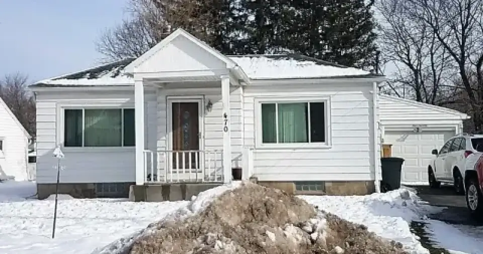A small white house with a front porch and snow-covered yard and driveway.
