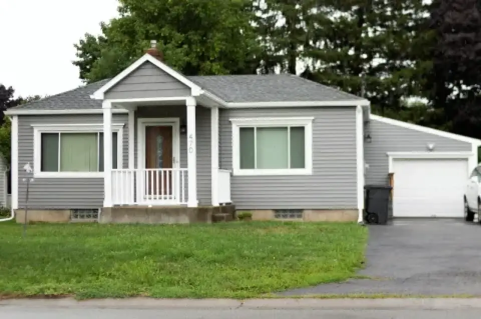 Single-story gray house with white trim, front porch, garage, and green lawn.