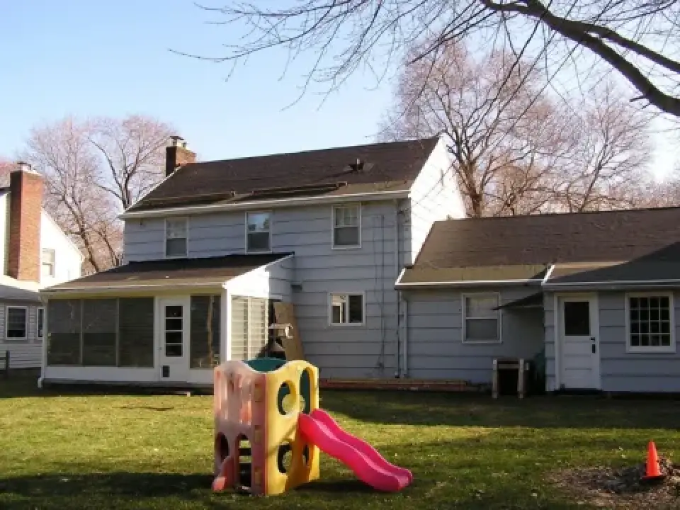 A small plastic playground slide sits in the backyard of a gray two-story house.
