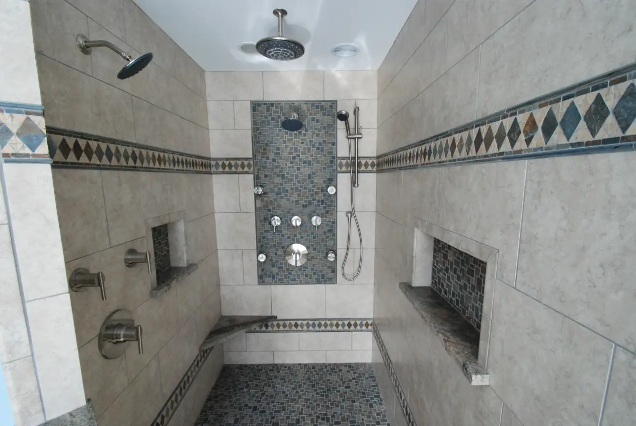 A modern shower with tiled walls, multiple showerheads, and decorative mosaic accents.