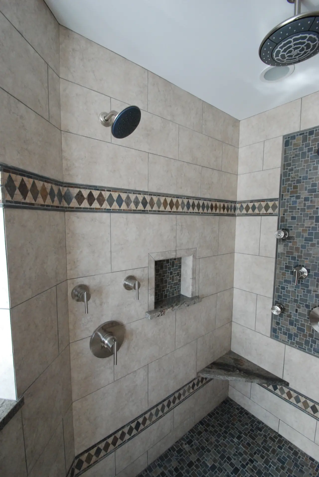 A modern shower with tiled walls, multiple showerheads, and a built-in niche for toiletries.