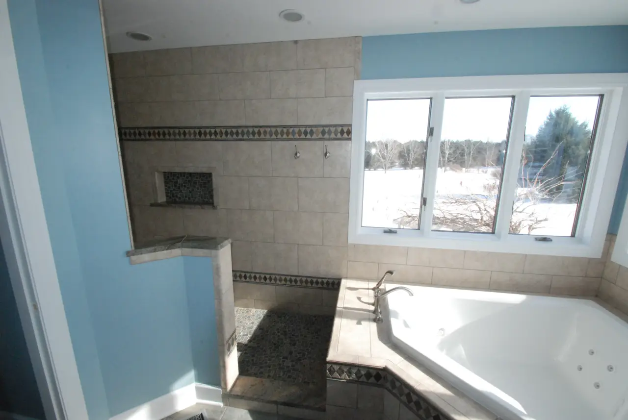 A spacious bathroom featuring a large tub, tiled shower area, and a window with a view of the outdoors.