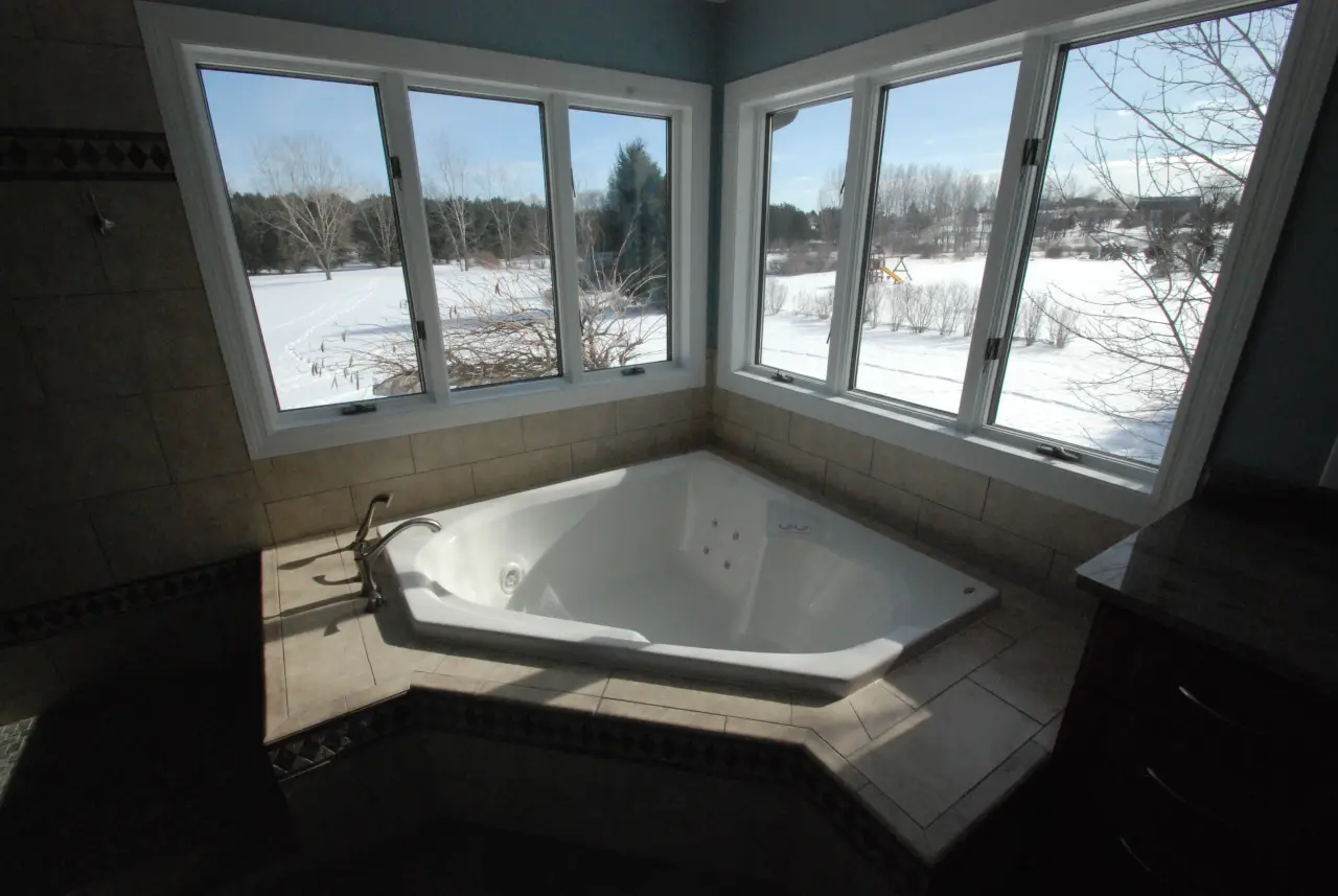 A spacious bathroom featuring a corner jacuzzi tub with large windows overlooking a snowy landscape.
