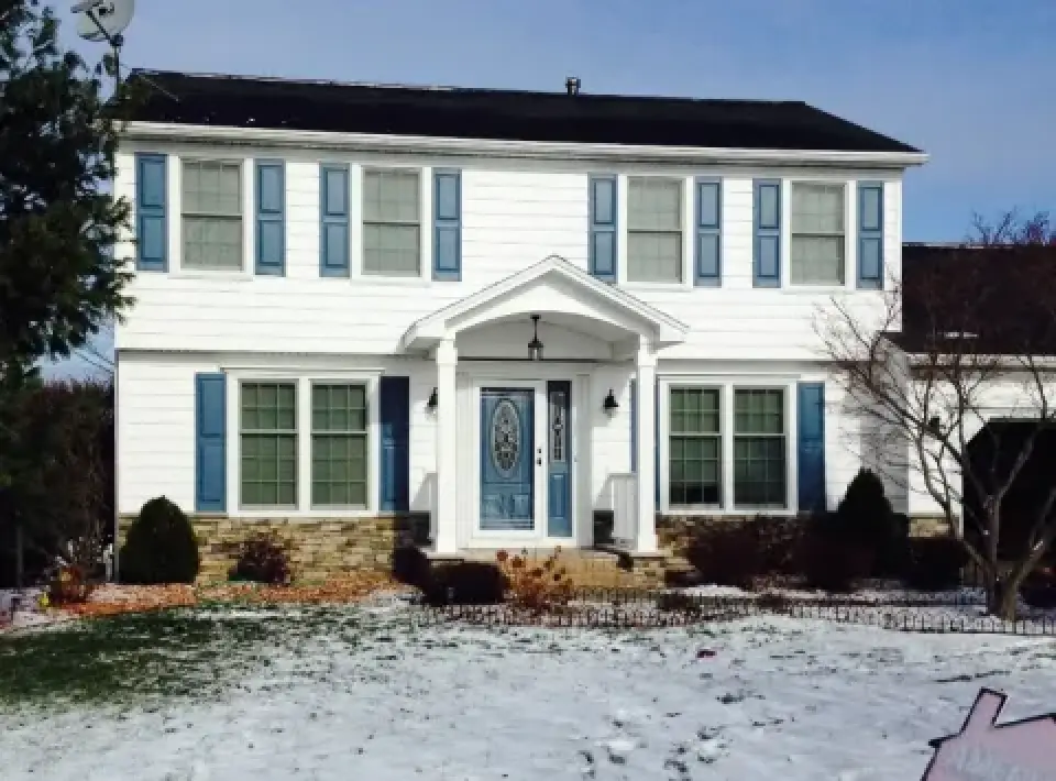 Two-story white house with blue shutters, snowy front yard, and a blue front door.
