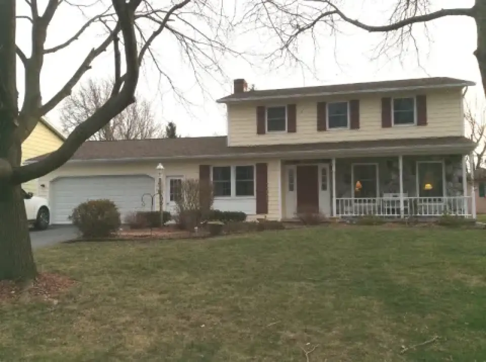 Two-story suburban house with yellow siding, red shutters, and a front porch, seen in winter.