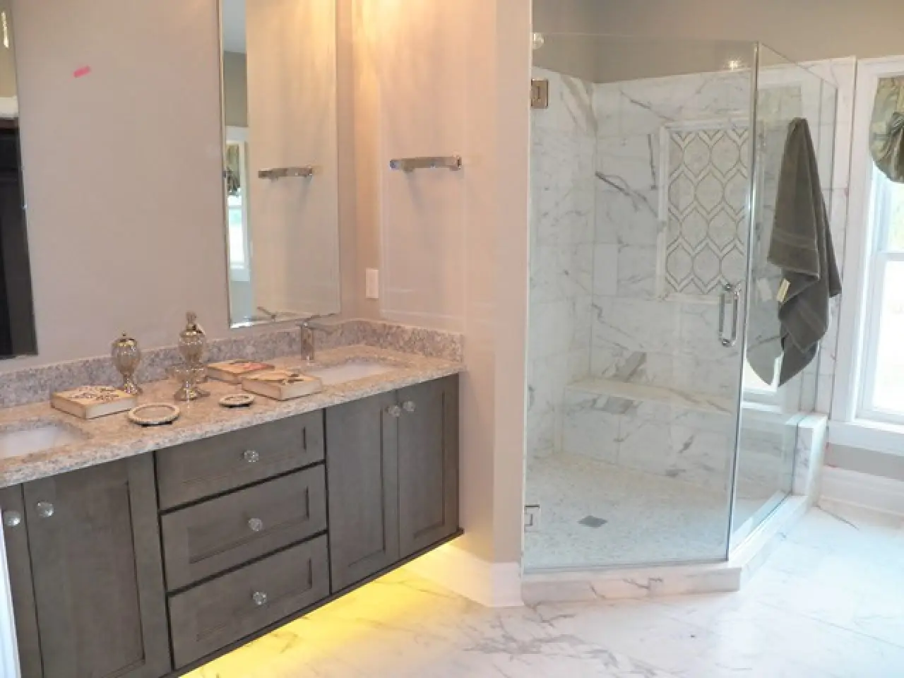 A modern bathroom featuring a double vanity with a granite countertop, a glass shower enclosure, and marble flooring.
