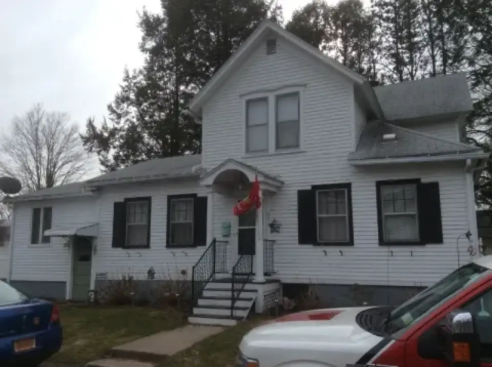 A white two-story house with black shutters and a red flag above the front steps.