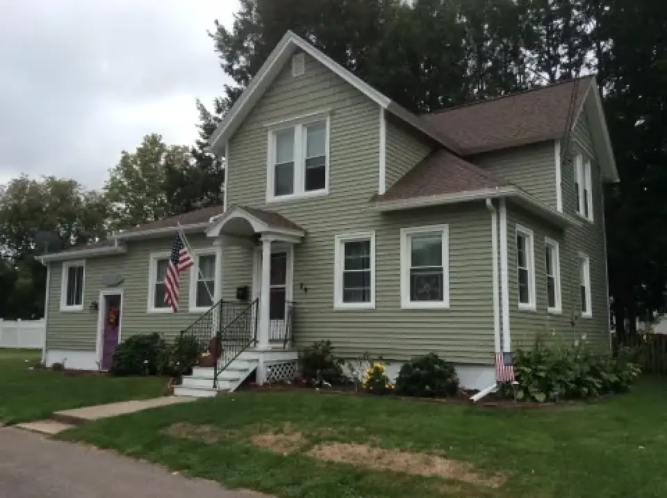 Light green two-story house with American flags, white trim, and a well-kept yard.