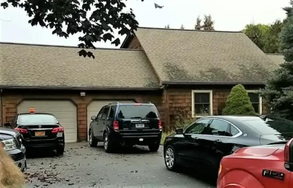Four cars parked in front of a two-car garage attached to a brown house with a shingled roof.