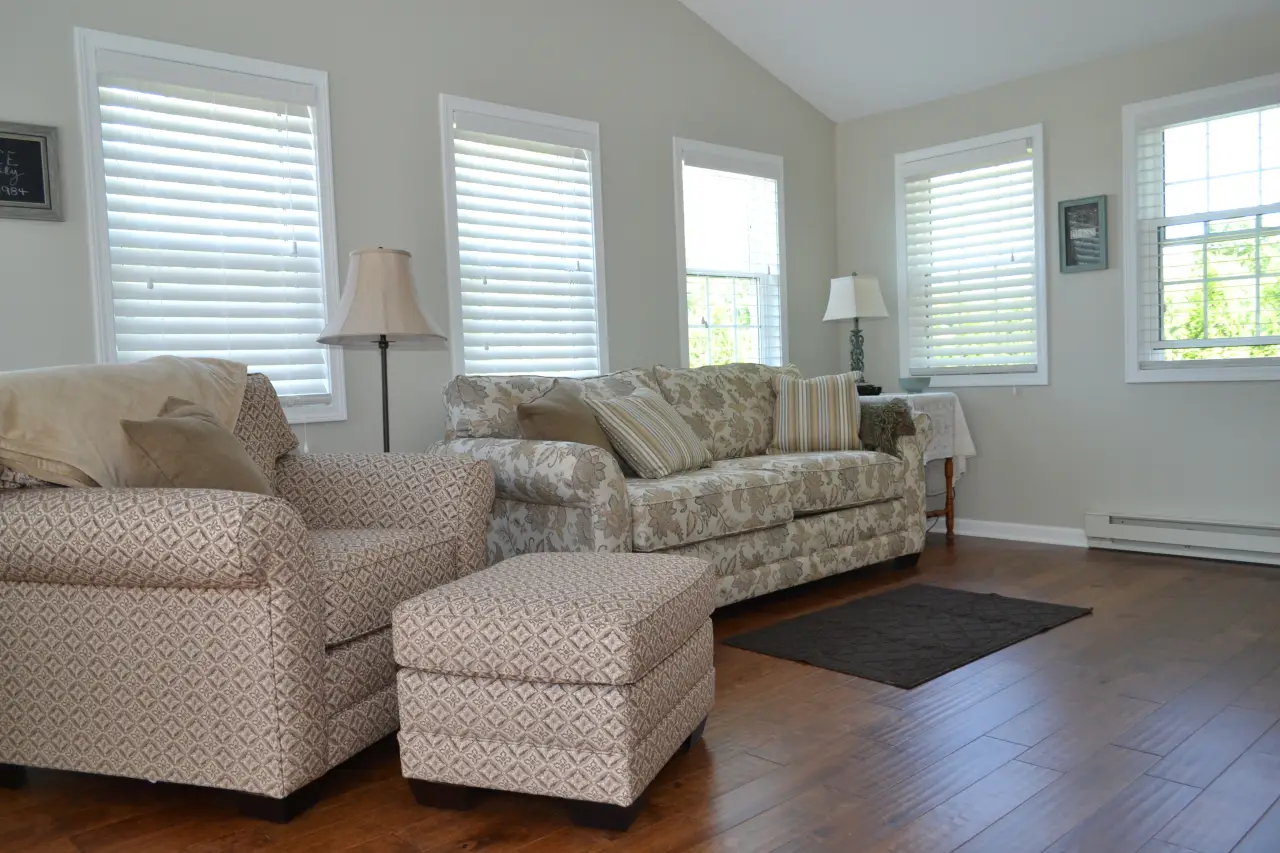 A cozy living room featuring a patterned sofa, armchair, and ottoman, with natural light from multiple windows.
