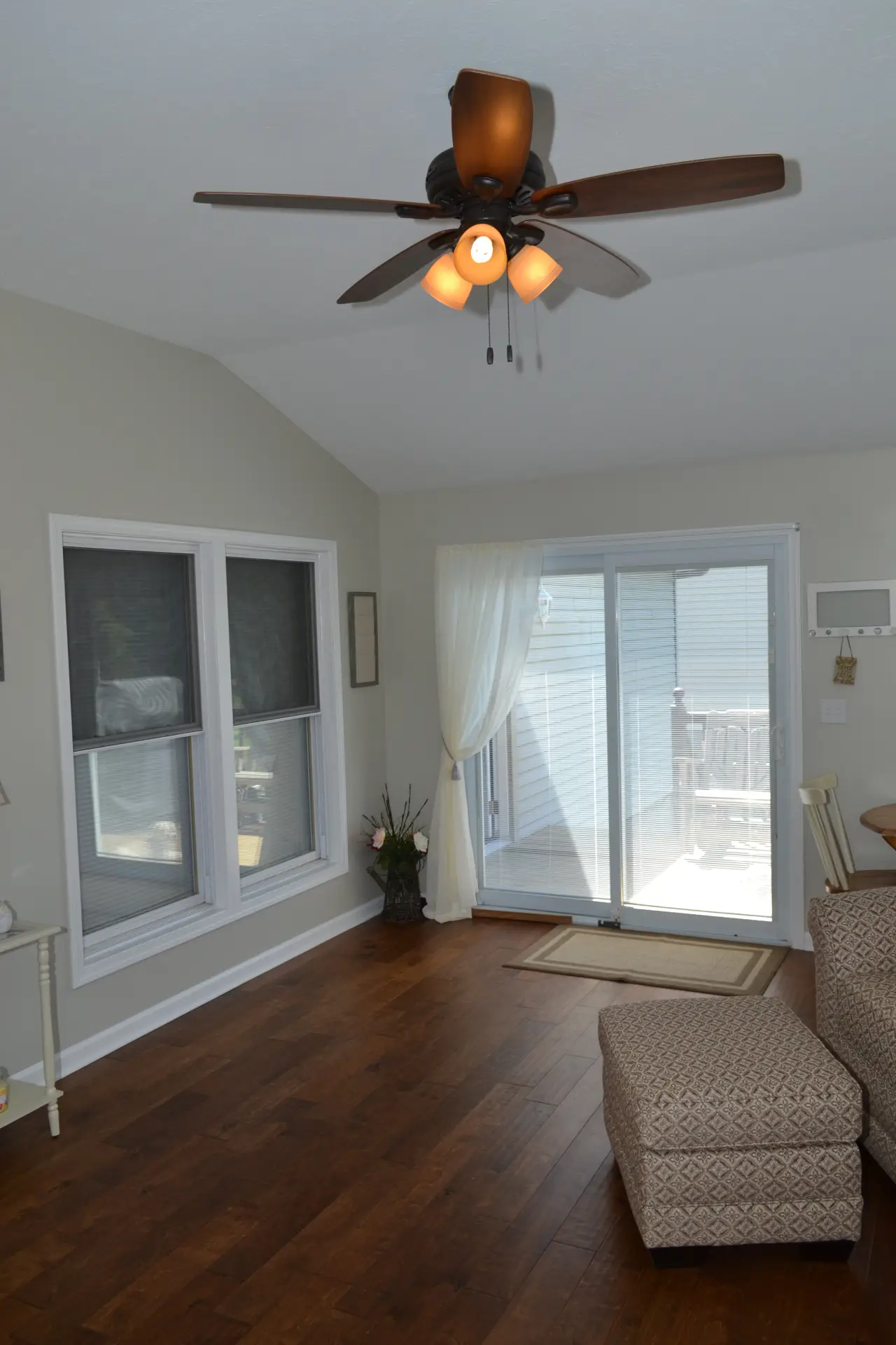 A bright living space featuring a ceiling fan, large windows, and a sliding glass door leading to a deck.