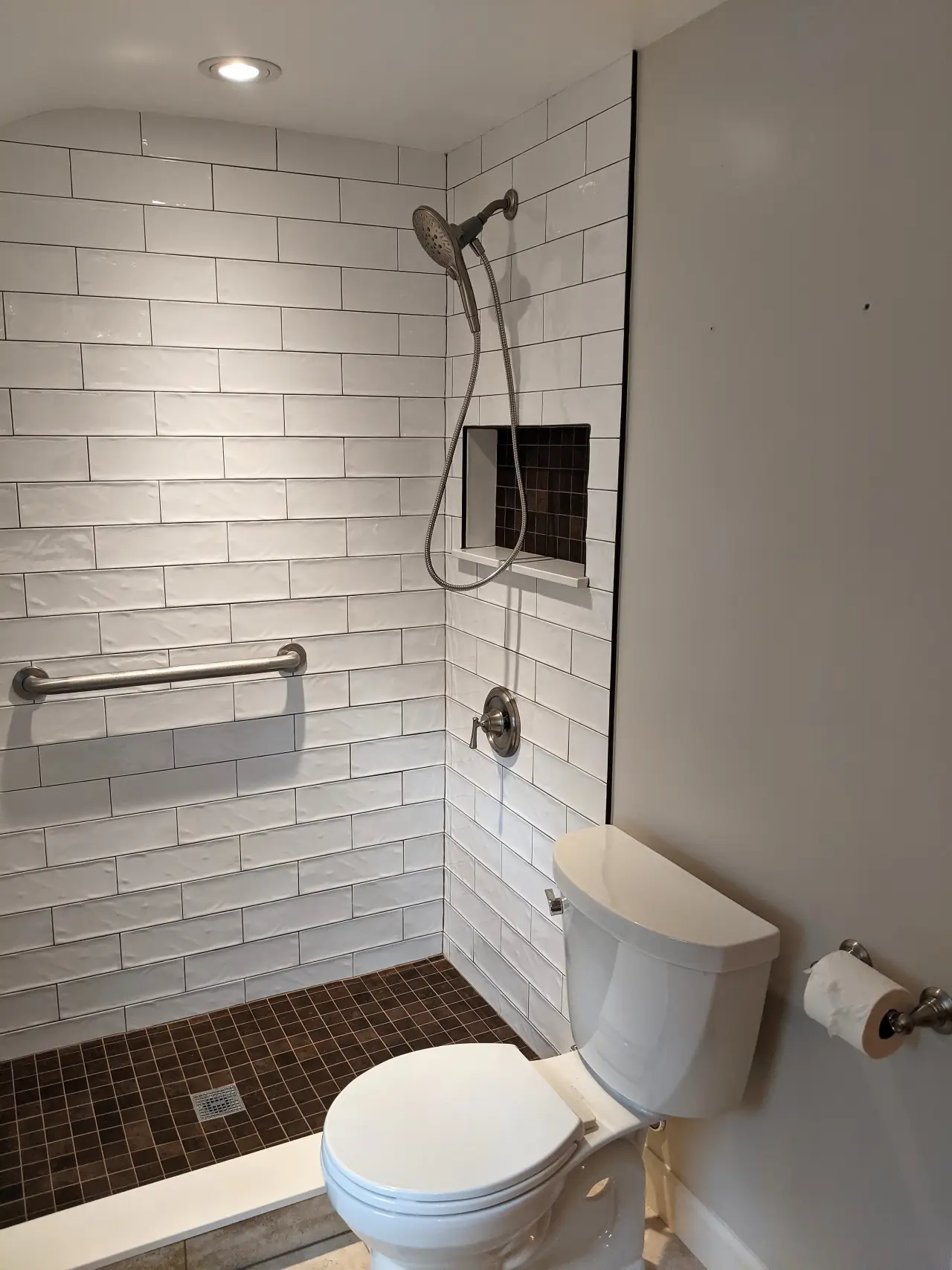 A modern bathroom featuring a shower with white tiled walls, a toilet, and a towel holder.