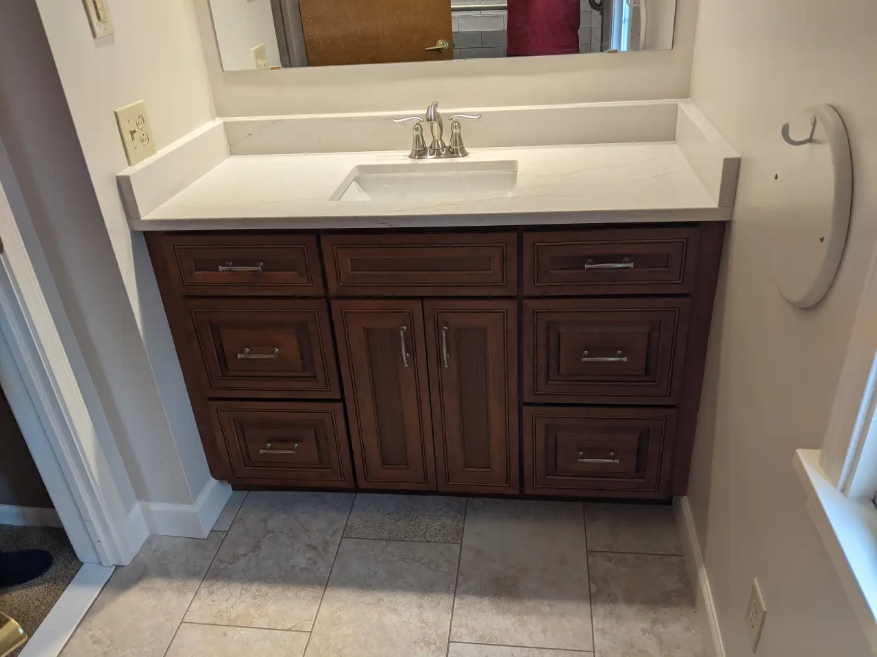 A wooden bathroom vanity with a white countertop and sink, featuring multiple drawers and a mirror above.