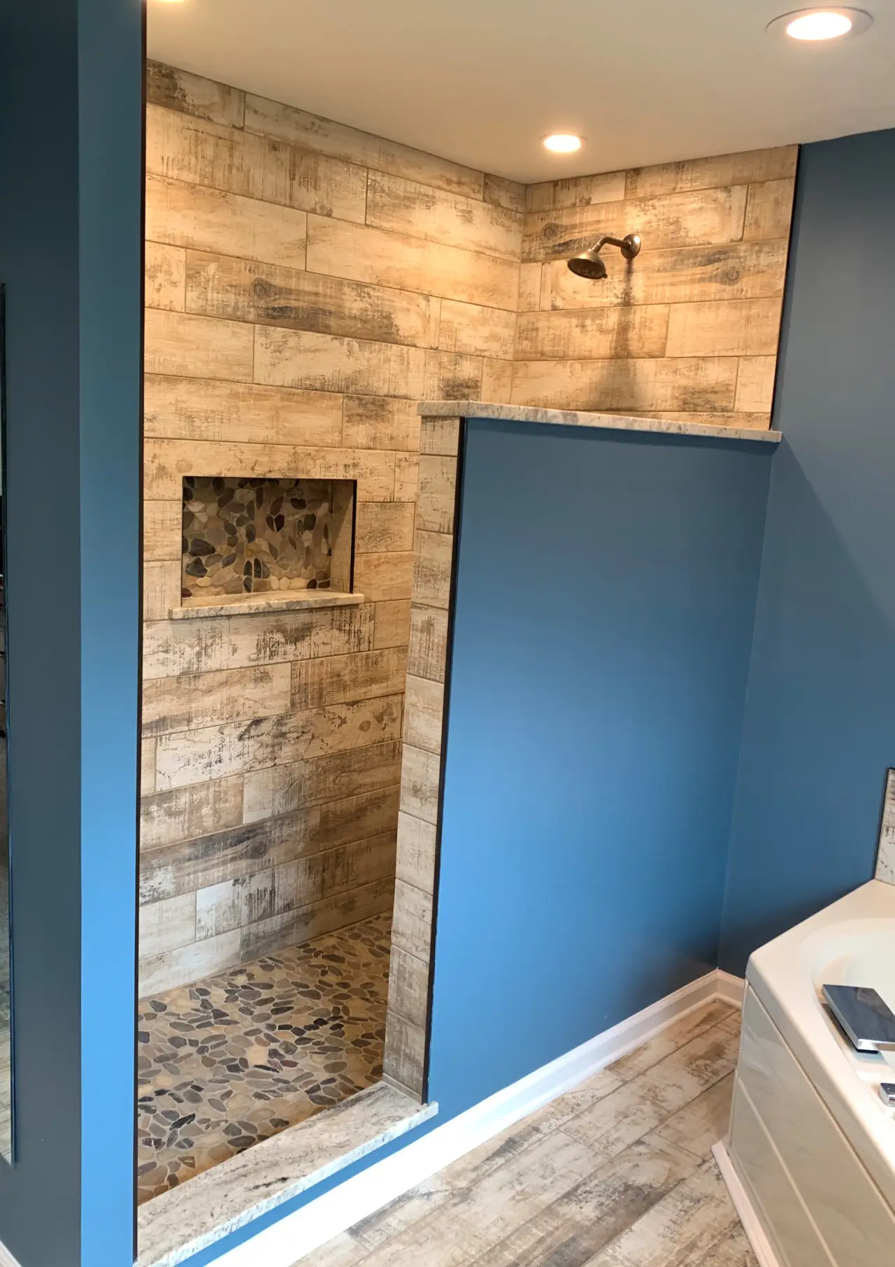 A modern bathroom featuring a walk-in shower with wooden tile walls, a pebble floor, and a blue accent wall.