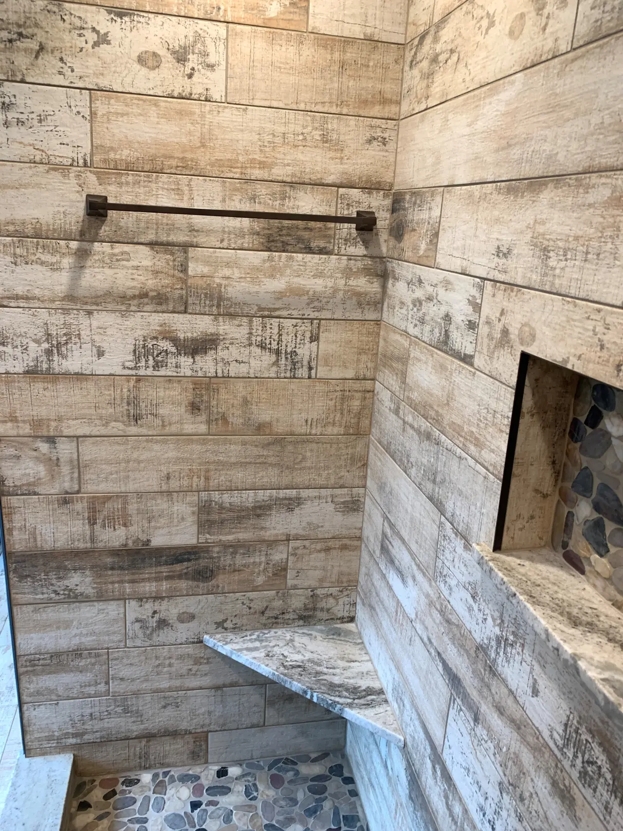 A modern shower with wooden-textured tiles, a stone bench, and a small niche for toiletries.