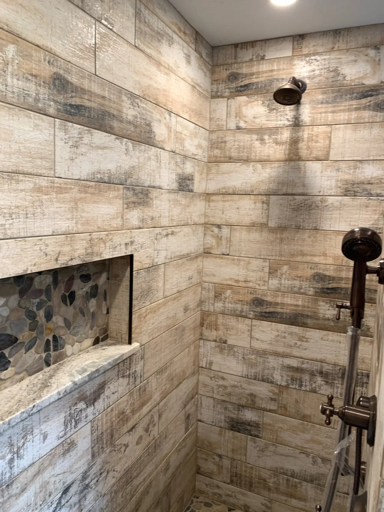 A modern shower with rustic wood-patterned tiles, a stone niche, and a sleek showerhead.
