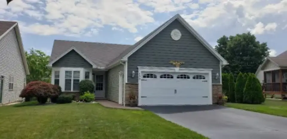 Single-story house with green siding, white trim, and a two-car garage on a neatly kept lawn.