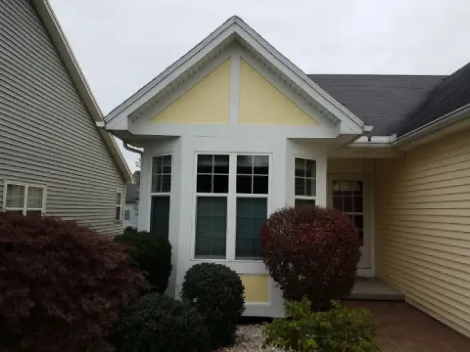 Small yellow and white house with shrubs and bushes in front, viewed on a cloudy day.