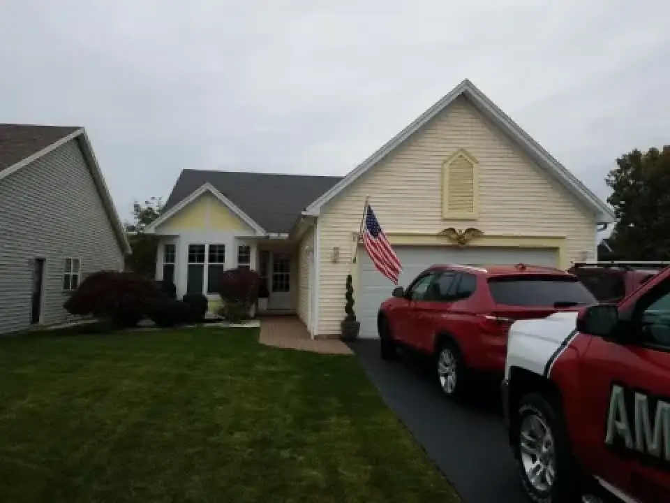 Yellow house with an American flag, red SUV, and red truck parked in the driveway.