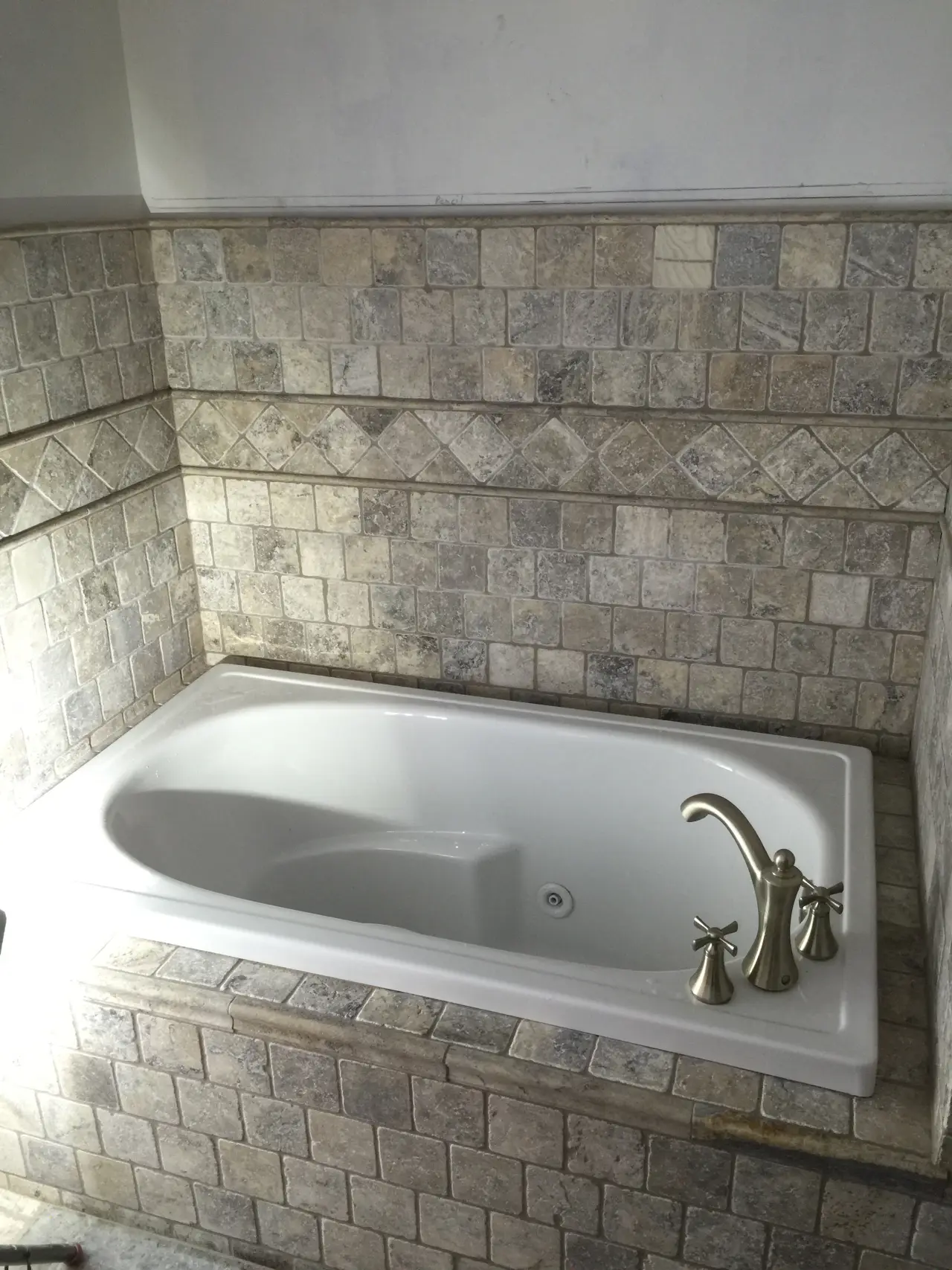 A modern bathtub with a sleek design, surrounded by textured stone tiles in neutral tones.