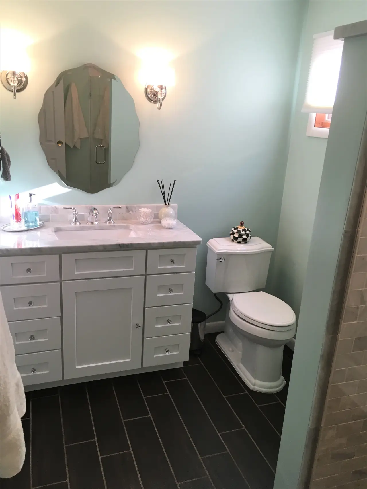 A modern bathroom featuring a white vanity with a marble countertop, a toilet, and light blue walls.