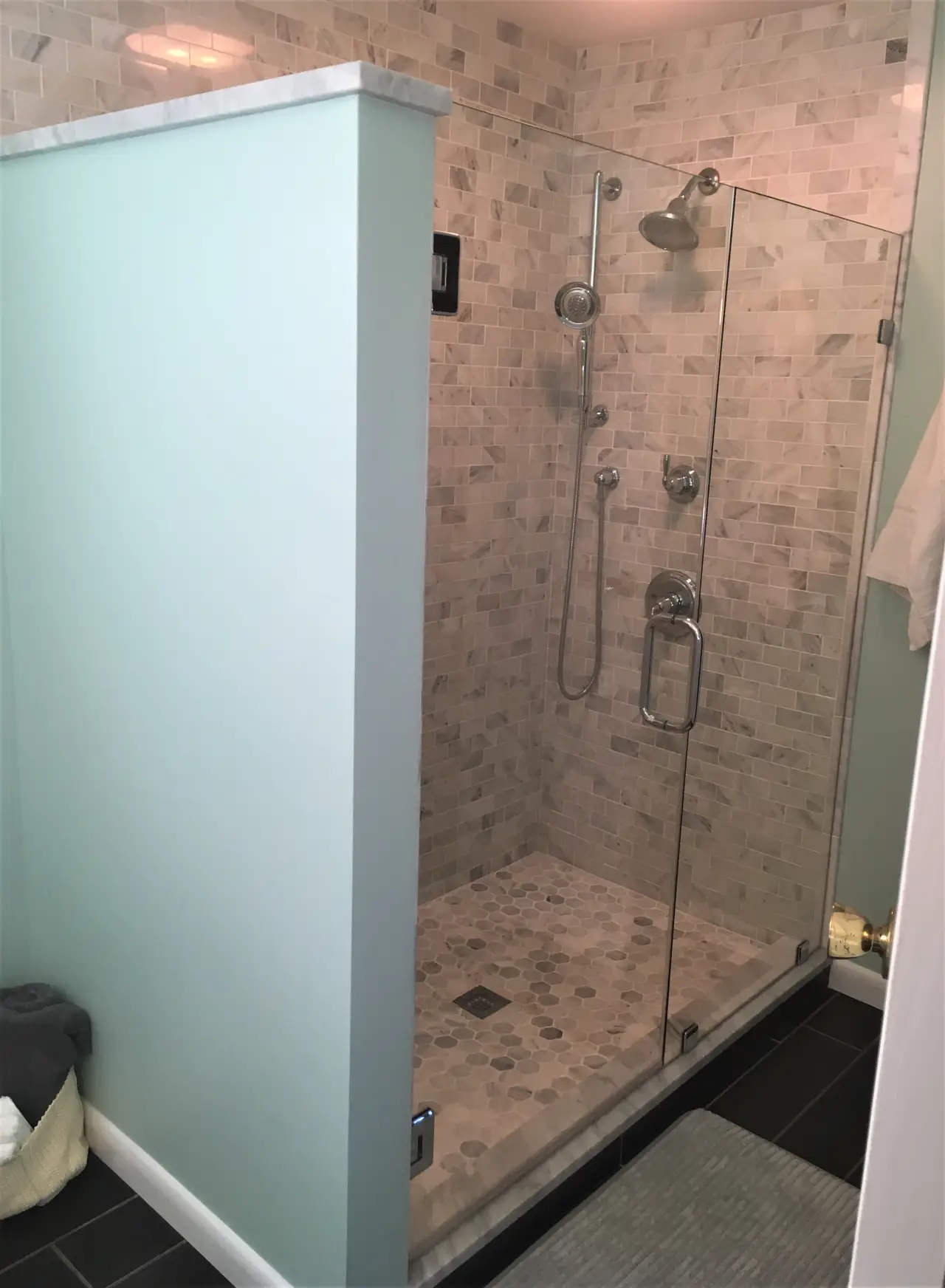 A modern shower with glass doors, featuring stone tiles and a rainfall showerhead, set against a light green wall.