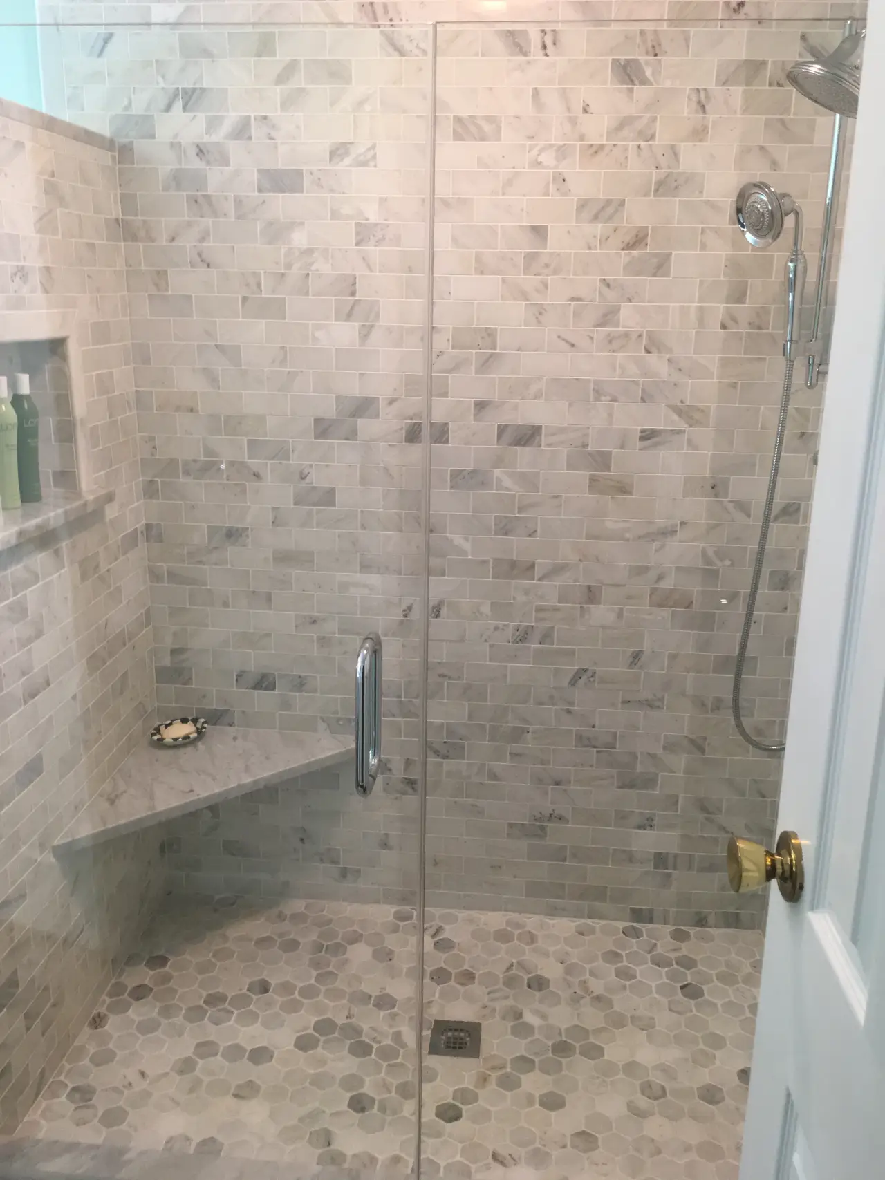A modern shower with glass walls, featuring marble tile and a built-in shelf with toiletries.