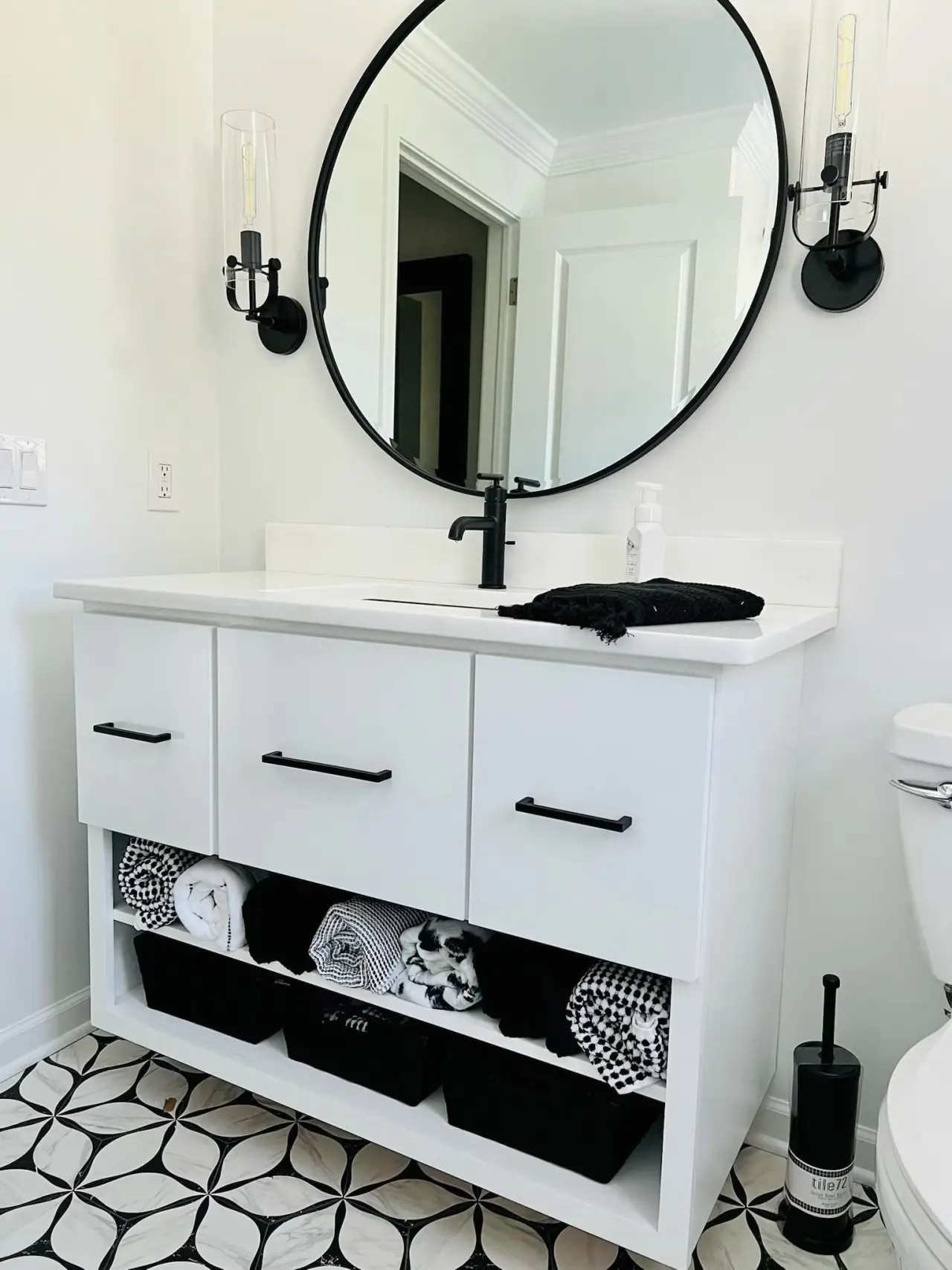 A modern bathroom vanity with a round mirror, black fixtures, and neatly organized towels in a stylish setting.
