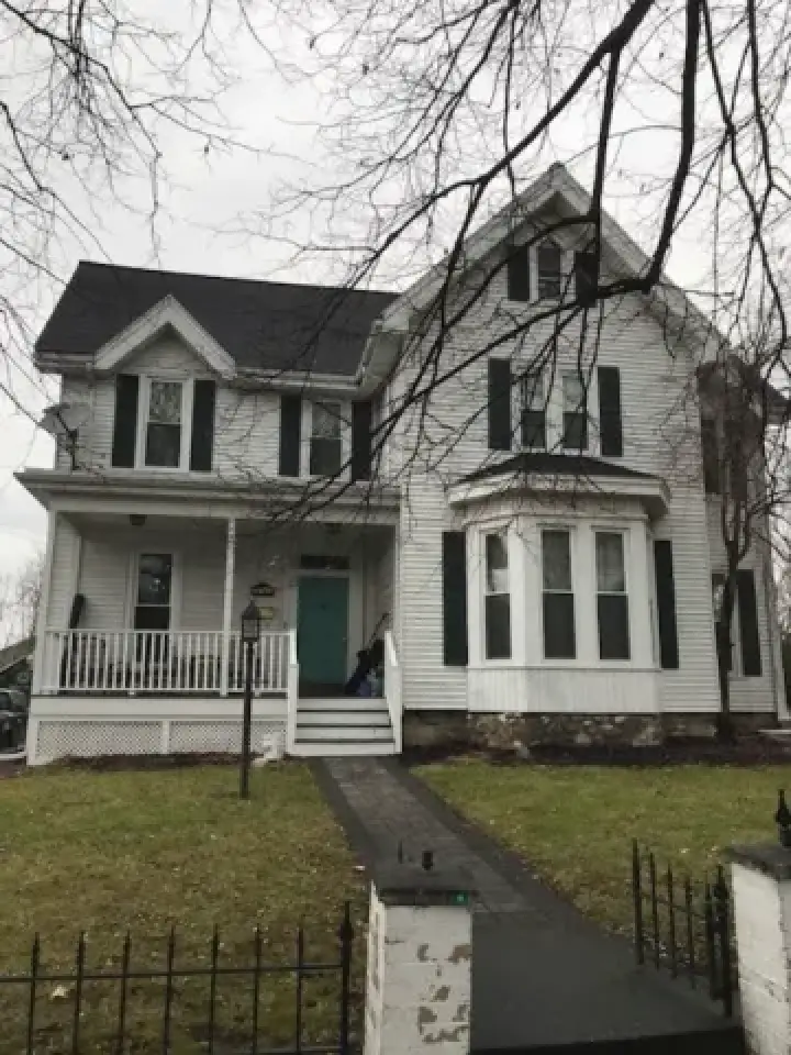 Two-story white Victorian house with black shutters, front porch, and a green front door.
