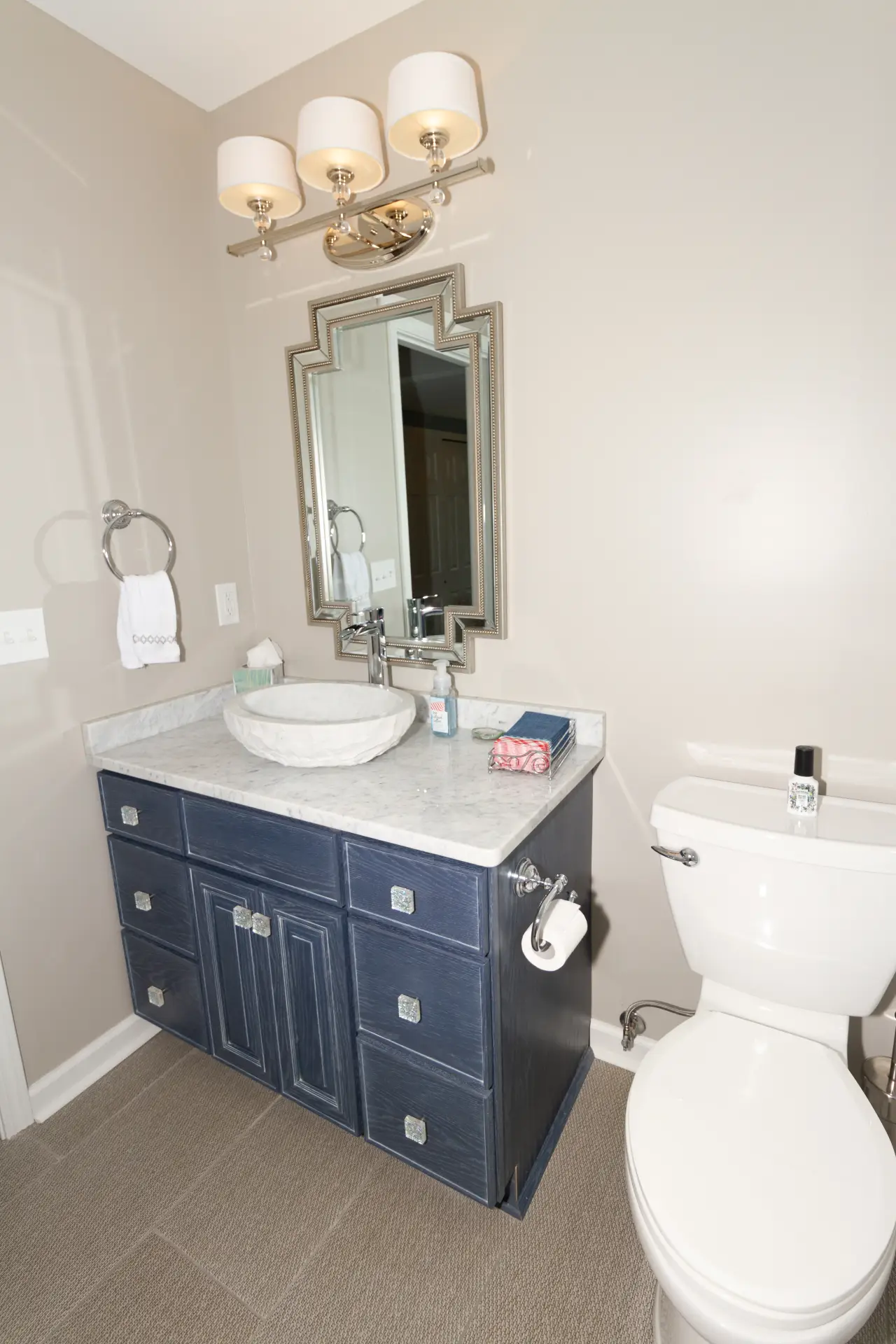 A modern bathroom featuring a dark blue vanity with a marble countertop, a round sink, and a toilet beside it.