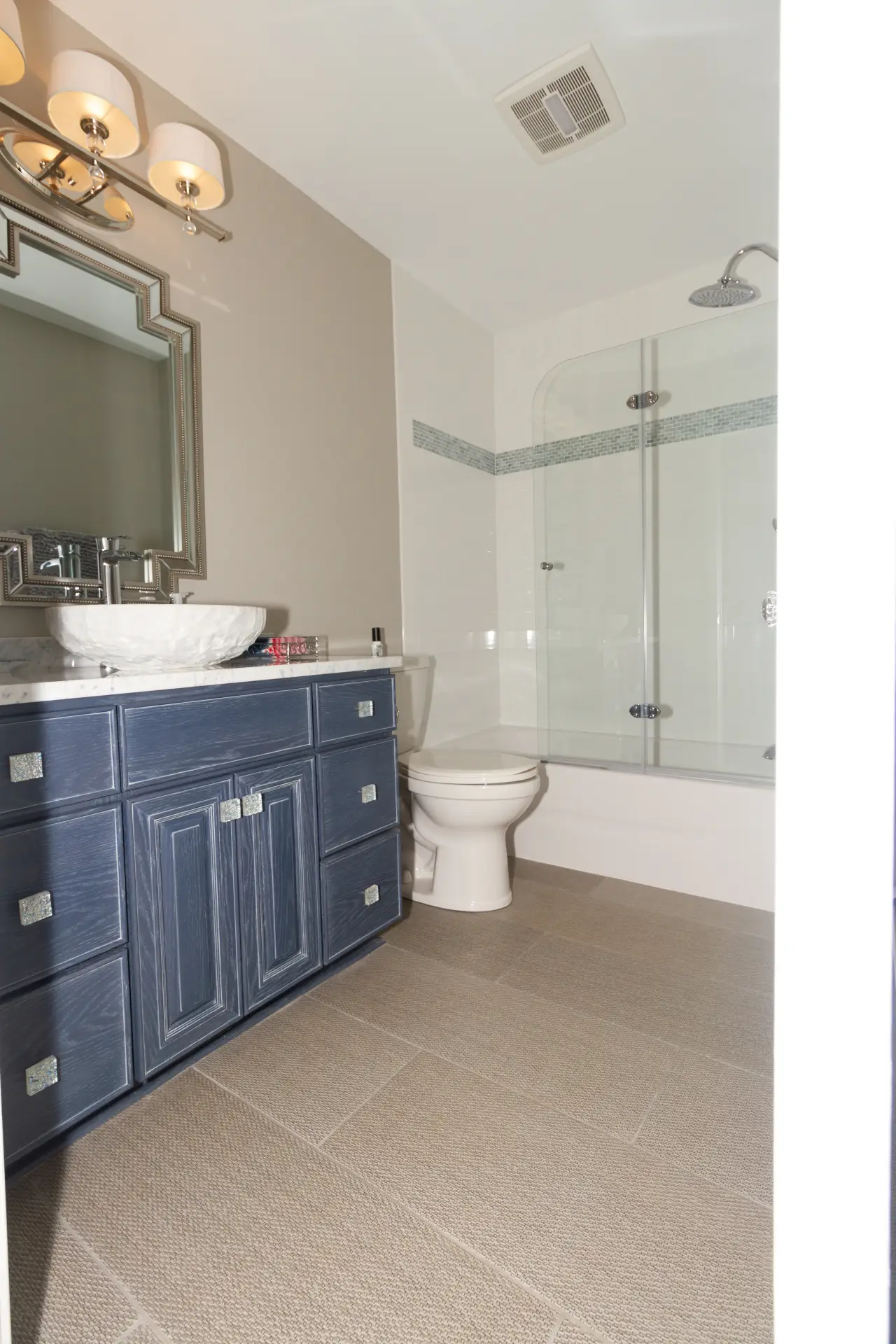 A modern bathroom featuring a blue vanity, a round sink, a glass shower, and neutral tile flooring.