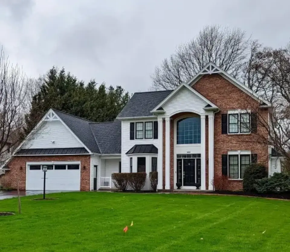 Two-story brick and white house with columns, large windows, and a neatly manicured lawn.