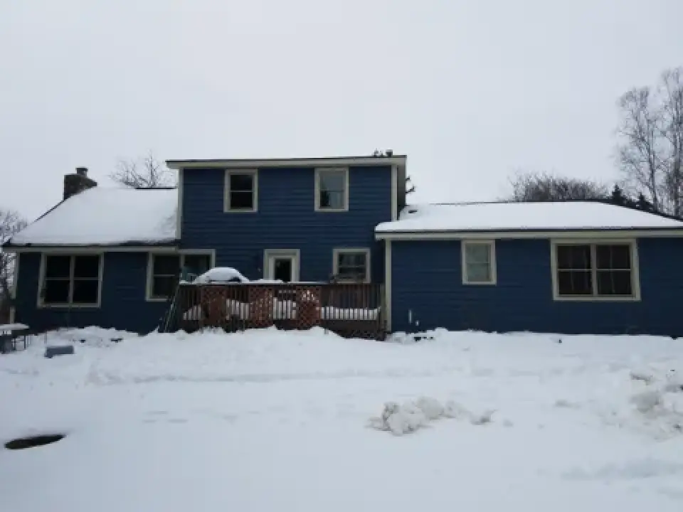 A blue house with snow-covered roof and yard, seen on a cloudy winter day.