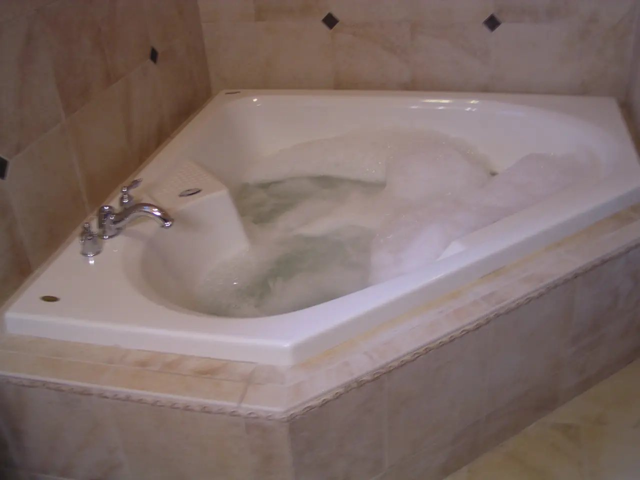 A white, corner jacuzzi tub filled with bubbles and water, set against a tiled wall.