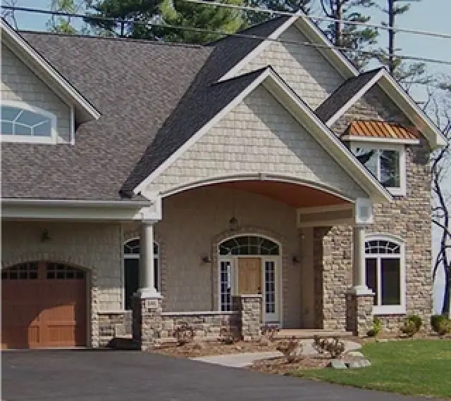 Modern house with stone and shingle exterior, arched entryway, and attached garage.