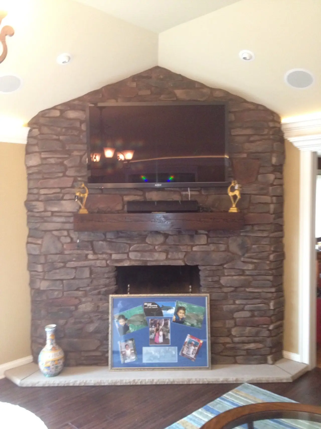 A stone fireplace with a mounted TV above it, featuring a wooden mantel and framed photos displayed below.