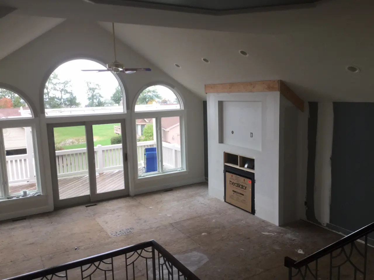 A spacious, unfinished living room with large arched windows, a fireplace, and wooden flooring.