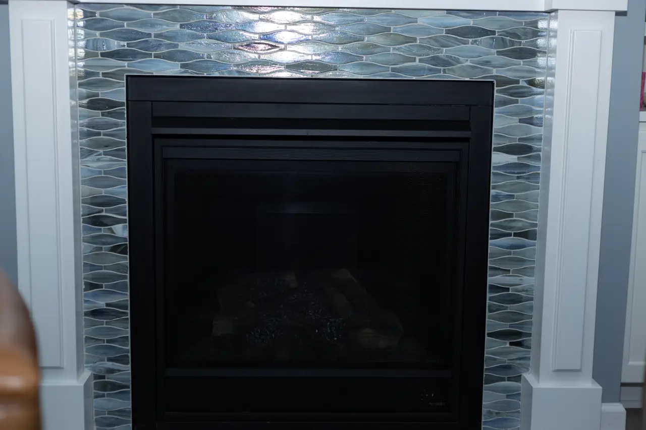 A modern fireplace with a sleek black frame, surrounded by a decorative mosaic tile design in shades of blue and gray.