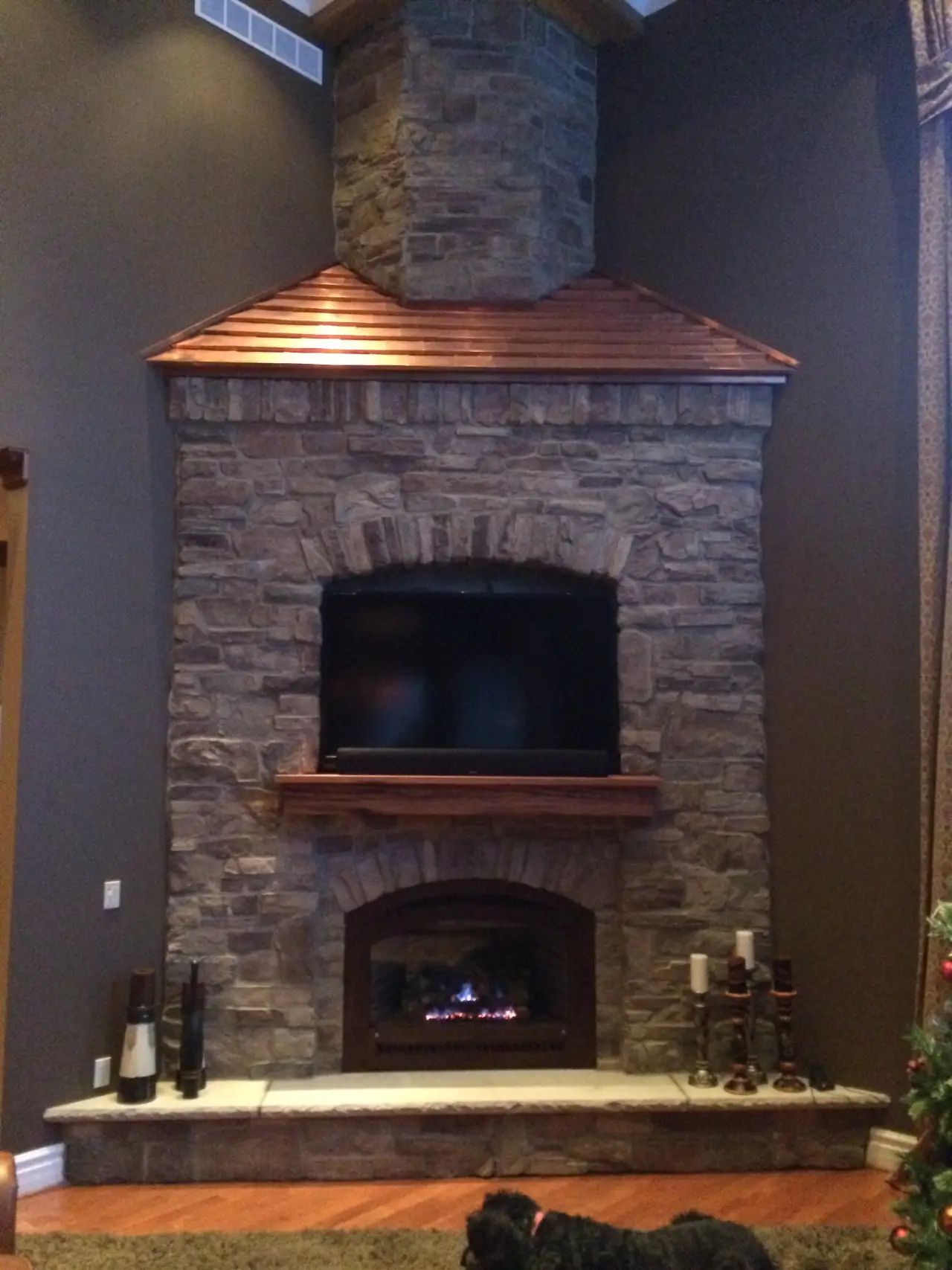 A stone fireplace with a wooden mantel and a TV above, featuring a cozy fire and decorative candles on the side.