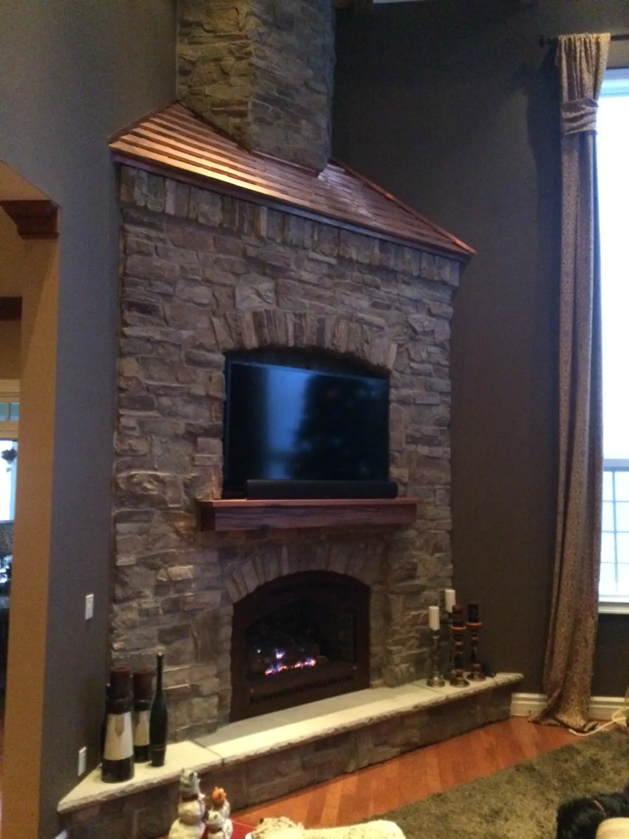 A stone fireplace with a wooden mantel, featuring a mounted TV above and decorative candles on the side.