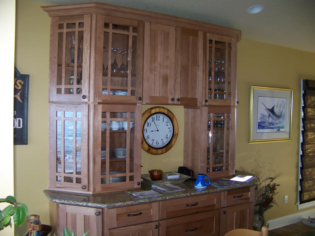 A wooden kitchen cabinet with glass doors, a round clock, and a countertop displaying various items.