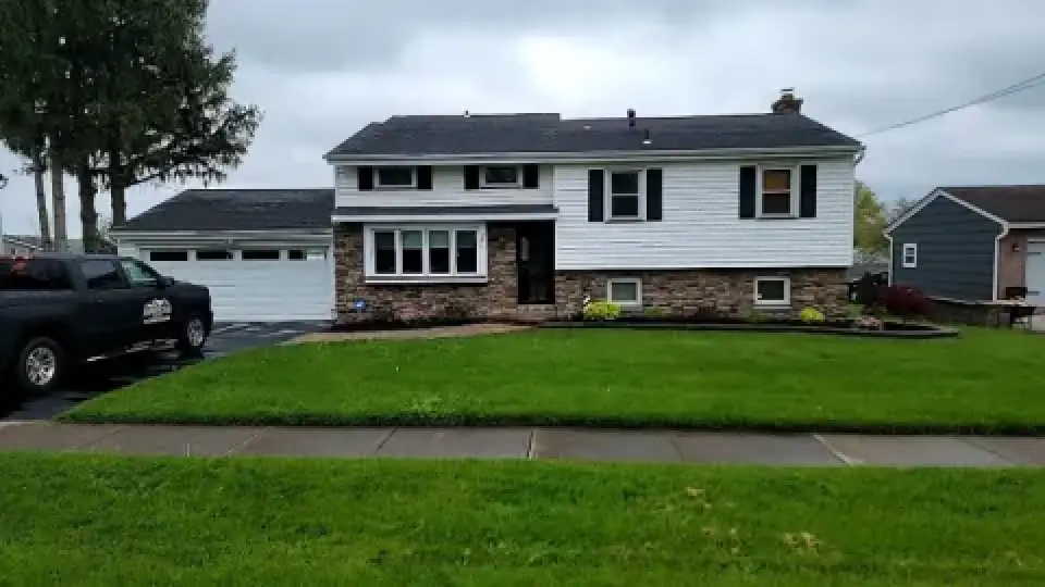 A split-level house with white siding, stone facade, green lawn, and a black truck in driveway.