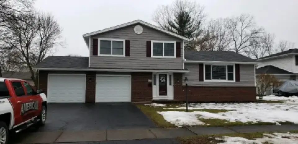 A two-story house with a red truck parked in the driveway and patches of snow on the lawn.