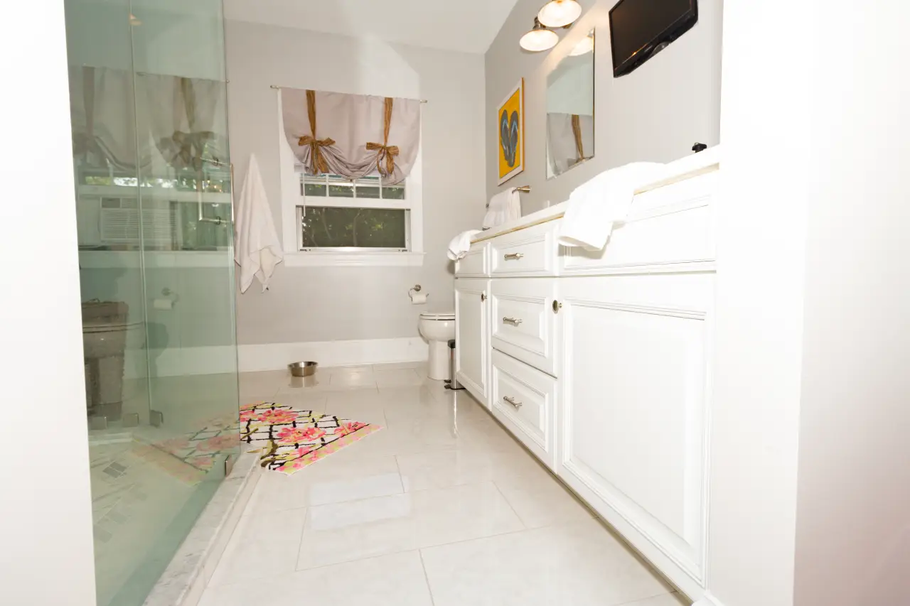 A bright bathroom featuring a glass shower, white cabinetry, and colorful decor on the floor.