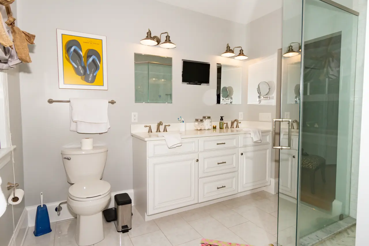 A modern bathroom featuring a double vanity, a shower with glass doors, a toilet, and decorative wall art.