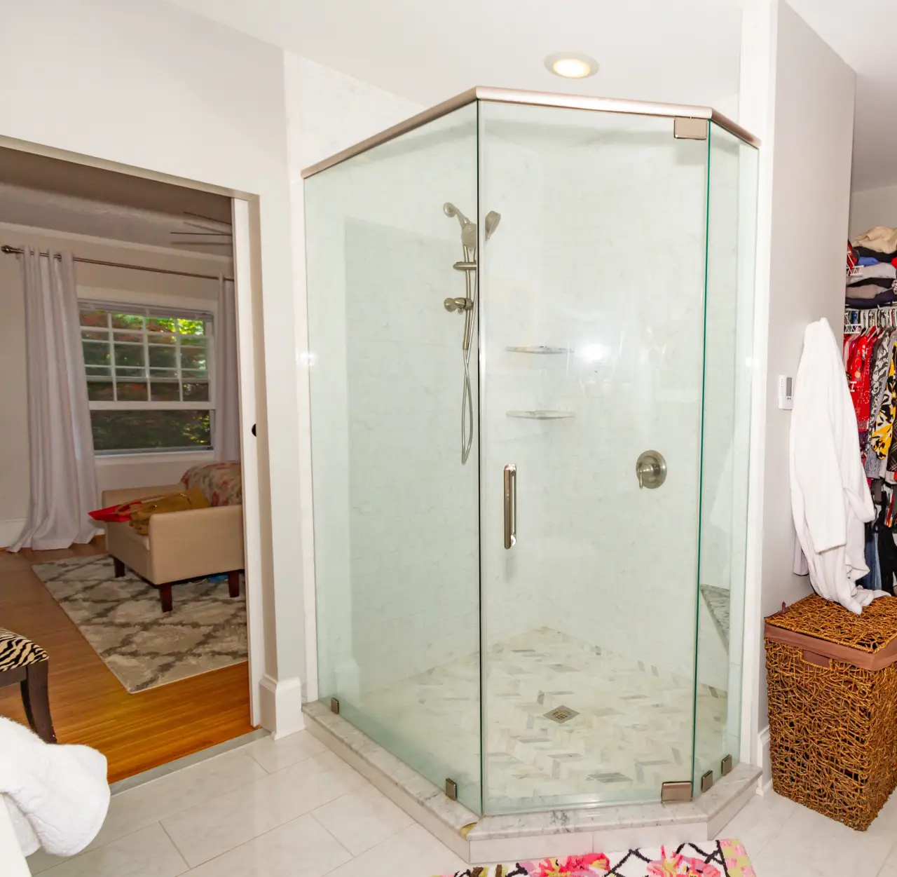 A modern glass shower enclosure with a marble floor, located in a bright bathroom near a cozy living area.