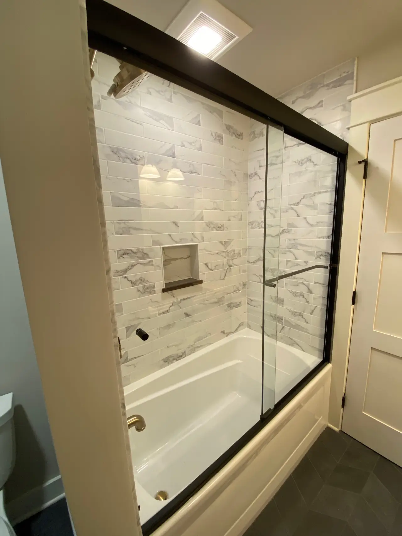 A modern bathroom featuring a glass shower enclosure, white tub, and marble-patterned tile walls.