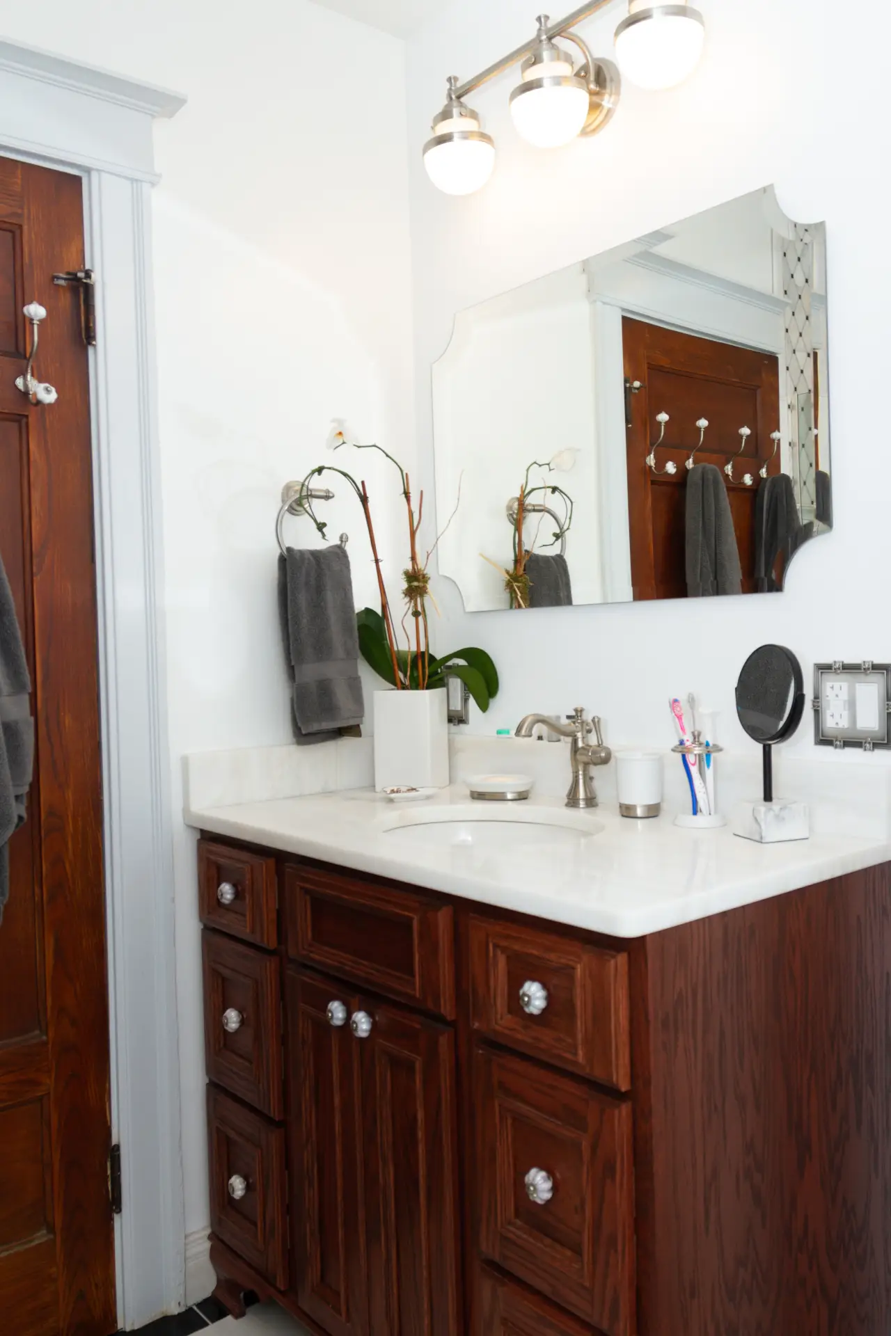 A modern bathroom featuring a wooden vanity, marble countertop, mirror, and decorative plants. Soft lighting and towels are visible.