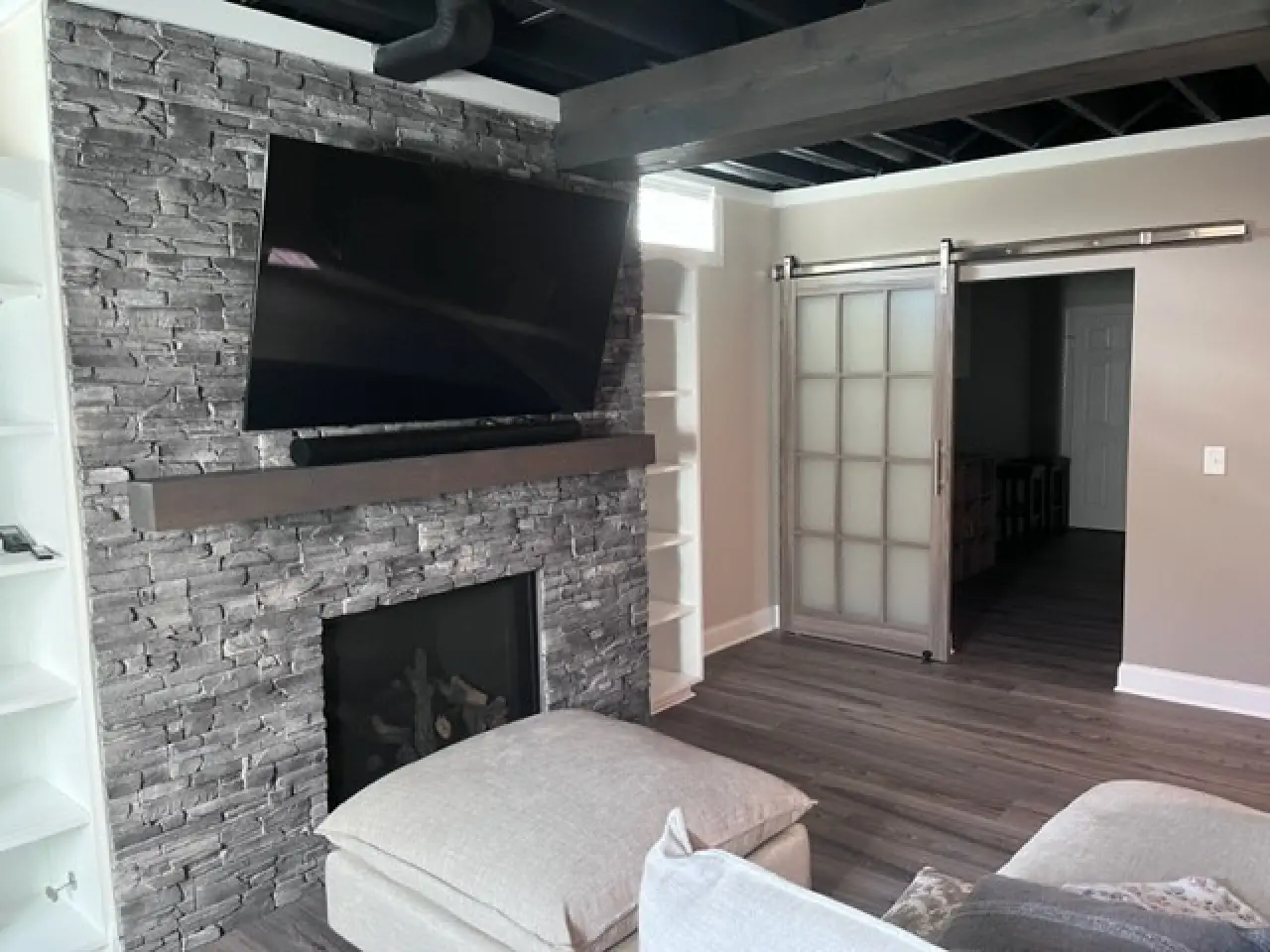 A modern living room featuring a stone accent wall with a mounted TV, a cozy sofa, and a sliding glass door leading to another room.
